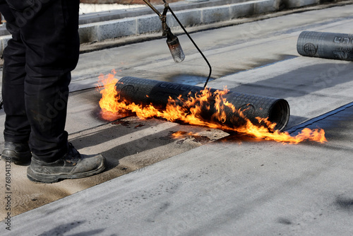 Professional construction workers using a blowtorch to glue modified bitumen roll sheet over a concrete road. © Silviu