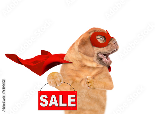 Barking Mastiff puppy with open mouth wearing superhero costume looking away on empty space and  showing signboard with labeled "sale". Isolated on white background