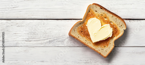 fetta di pane tostato con noce di burro a forma di cuore, superficie tavolo in legno bianco
