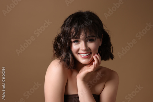 Portrait of beautiful young woman with wavy hairstyle on brown background