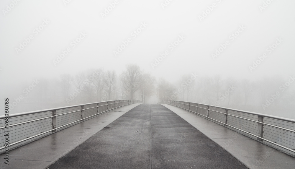 Bridge to fogland. Bridge over a river disappearing in a dense fog - low visibility on November morning. Symmetric vanishing point view of the empty bridge.