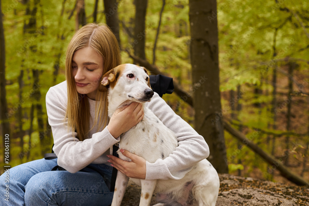 Gentle forest scene with a blonde woman explorer hugging her dog, caring for her pet's comfort Gentle forest scene with a blonde woman explorer hugging her dog, caring for her pet's comfort