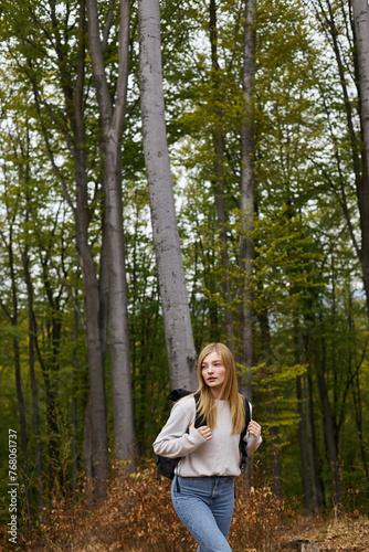 Enthusiastic and blonde girl in green forest wearing sweater and jeans, exploring scenic view © LIGHTFIELD STUDIOS
