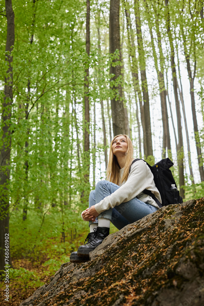 Photo of female hiker hugging her legs wearing sweater, jeans and hiking boots sitting in forest Photo of female hiker hugging her legs wearing sweater, jeans and hiking boots sitting in forest