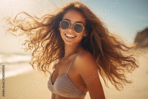 Smiling young beautiful woman with a bikini, wearing sunglasses on the beach, flowing hair, enjoying her summer vacation holiday travel © Daniel