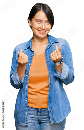 Young beautiful hispanic woman with short hair wearing casual denim jacket doing money gesture with hands, asking for salary payment, millionaire business
