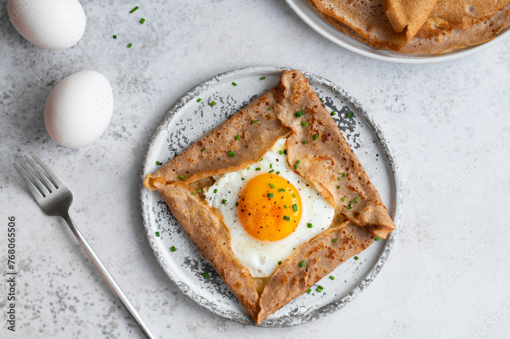 Homemade buckwheat crepes. Galettes Bretonnes with cheese and fried egg on a grey background. Traditional French cuisine. Homemade buckwheat crepes. Galettes Bretonnes with cheese and fried egg on a grey background. Traditional French cuisine.