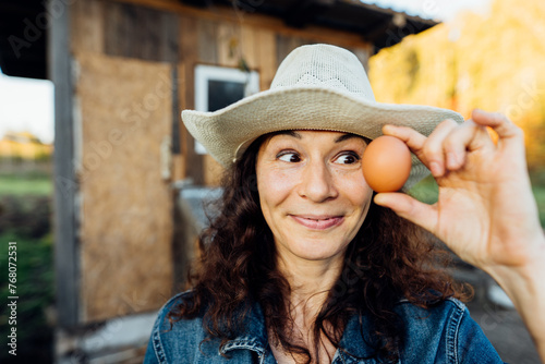 Portrait of funny joyful farmer woman holding fresh egg near her face. While enjoying farming, a female farmer holds a fresh egg Happy moment of collecting eggs