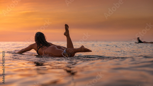 Candid view of a woman surfer heading out to catch waves at sunset