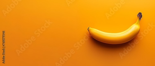   A ripe banana rests atop an orange surface, beside a banana peel stacked on top of another banana peel © Jevjenijs