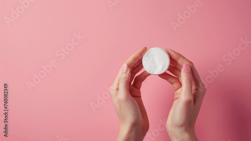 Skincare routine step for healthy skin - Woman hands holding facial cotton pad, foam, essential oil, serum, lotion and eye cream packaging on pink background. Beauty and cosmetic concept. Copy space. photo