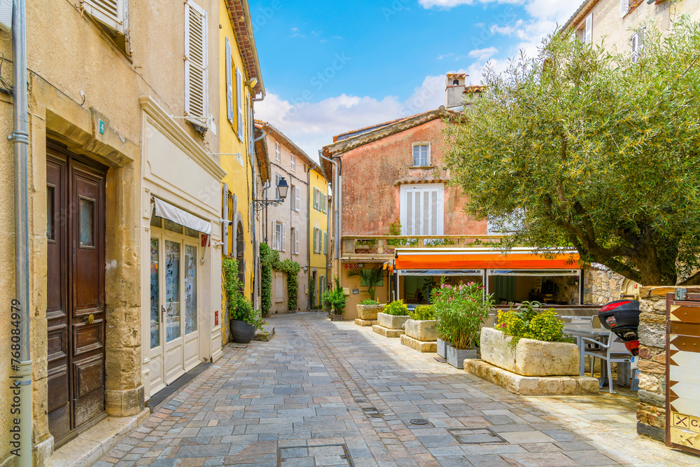 Obraz premium A small square leading to a narrow alley full of shops and sidewalk cafes in the historic old town of the hilltop medieval village of Grimaud, France in Provence.