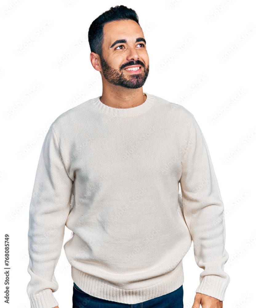 Young hispanic man with beard wearing casual white sweater looking away to side with smile on face, natural expression. laughing confident. Young hispanic man with beard wearing casual white sweater looking away to side with smile on face, natural expression. laughing confident.