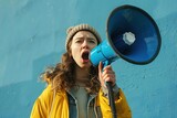 Capturing the fervor of activism, a young woman passionately shouts into a megaphone against a bold blue backdrop