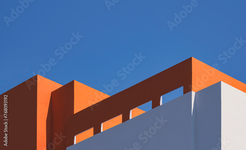 Geometric architecture pattern of high section of modern orange and white building with sunlight and shadow on rooftop surface against blue clear sky background in minimal style, Low angle view