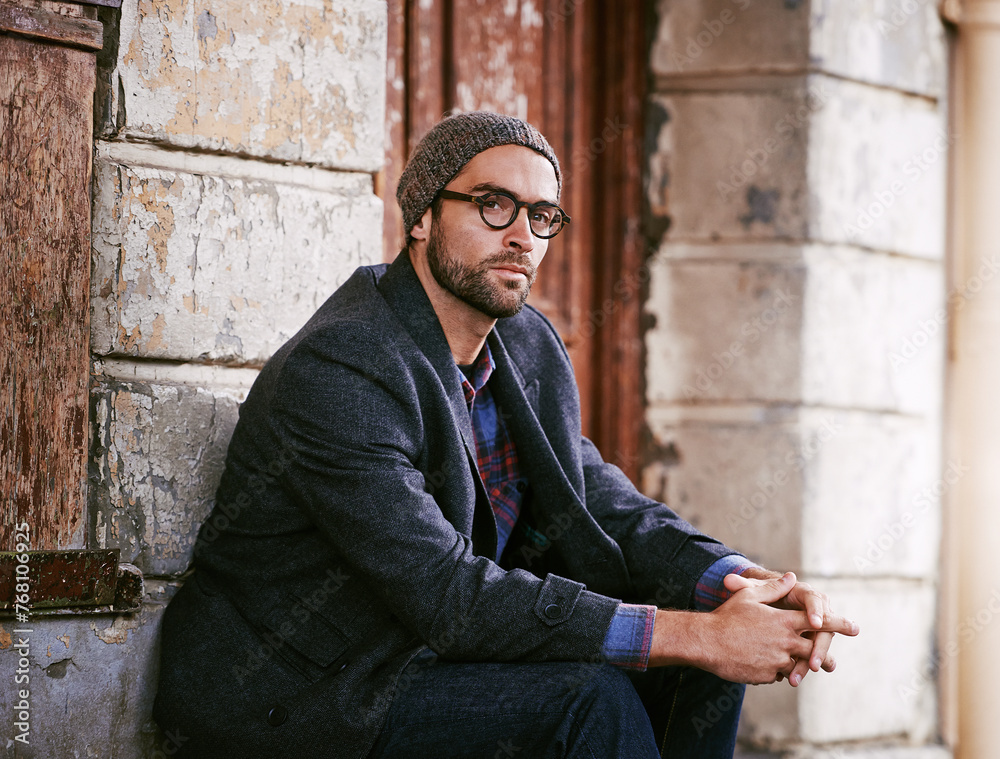 Obraz premium Fashion, portrait or man in town by a wall or building in casual clothes, style or edgy coat for a winter outfit. Glasses, cool model or stylish male person in modern beanie or trendy jacket in Italy