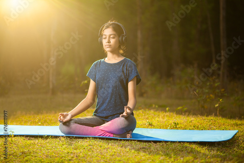 asian athlete women meditating in a zen-like position or padmasana pose while listening to music on a headphone at sunrise photo