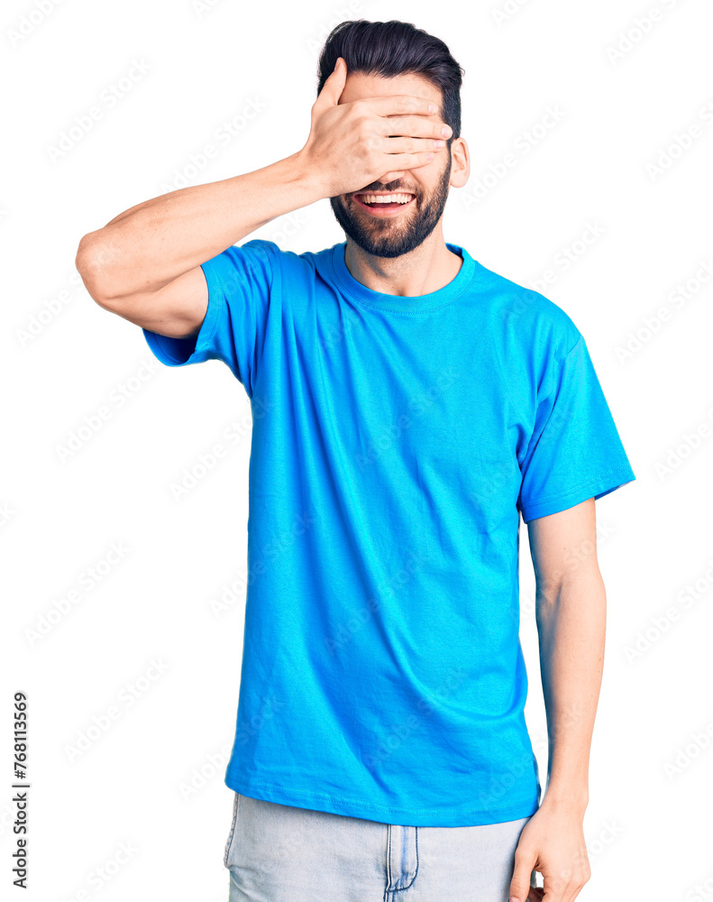 Young handsome man with beard wearing casual t-shirt smiling and laughing with hand on face covering eyes for surprise. blind concept. Young handsome man with beard wearing casual t-shirt smiling and laughing with hand on face covering eyes for surprise. blind concept.