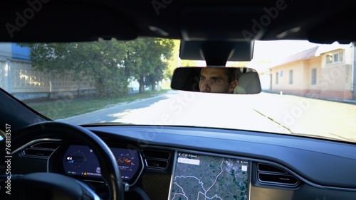 Fototapeta Naklejka Na Ścianę i Meble -  Eyes of male driver reflecting of rearview mirror during riding electrical auto. Confident man driving a modern car at city. Young guy looking concentrated to urban road during operating vehicle