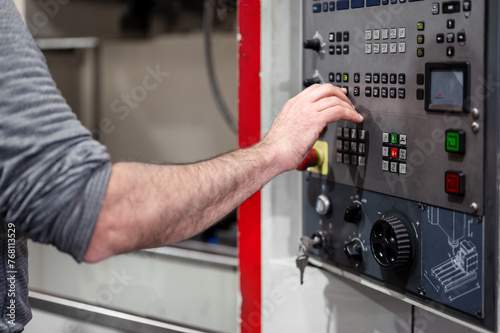 Worker pressing buttons on CNC machine control board in factory. High quality photography.