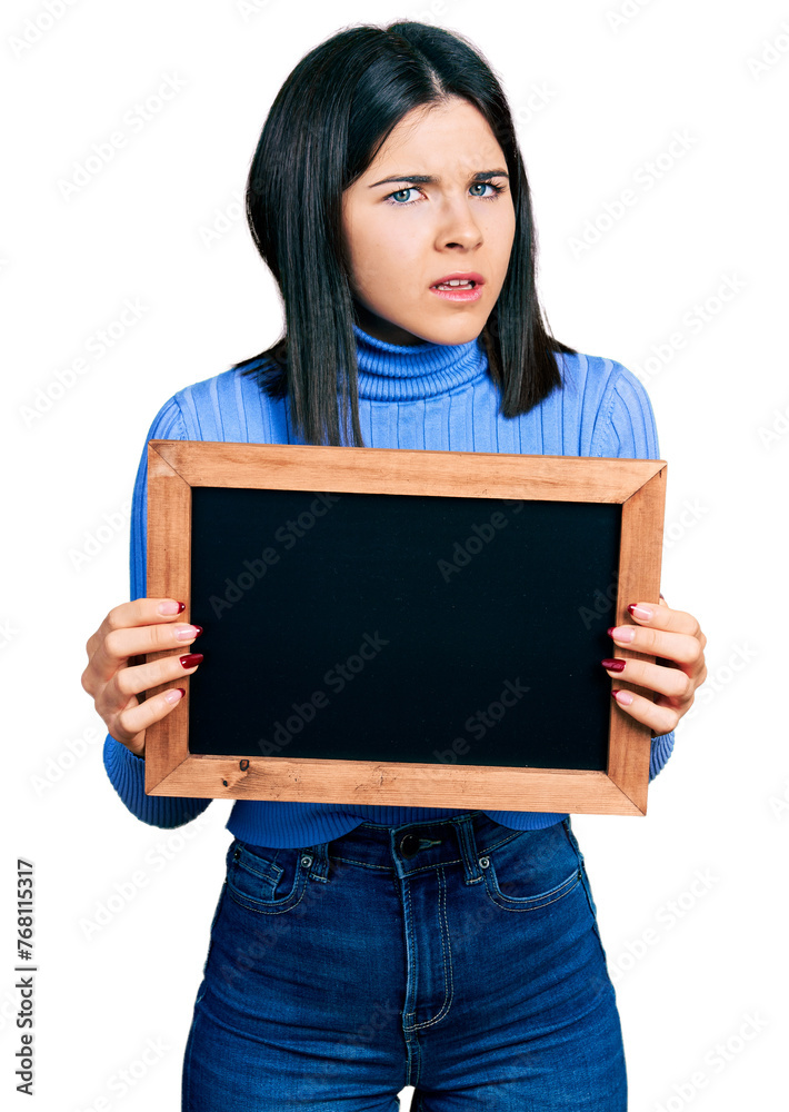 Young brunette woman with blue eyes holding blackboard clueless and confused expression. doubt concept. Young brunette woman with blue eyes holding blackboard clueless and confused expression. doubt concept.