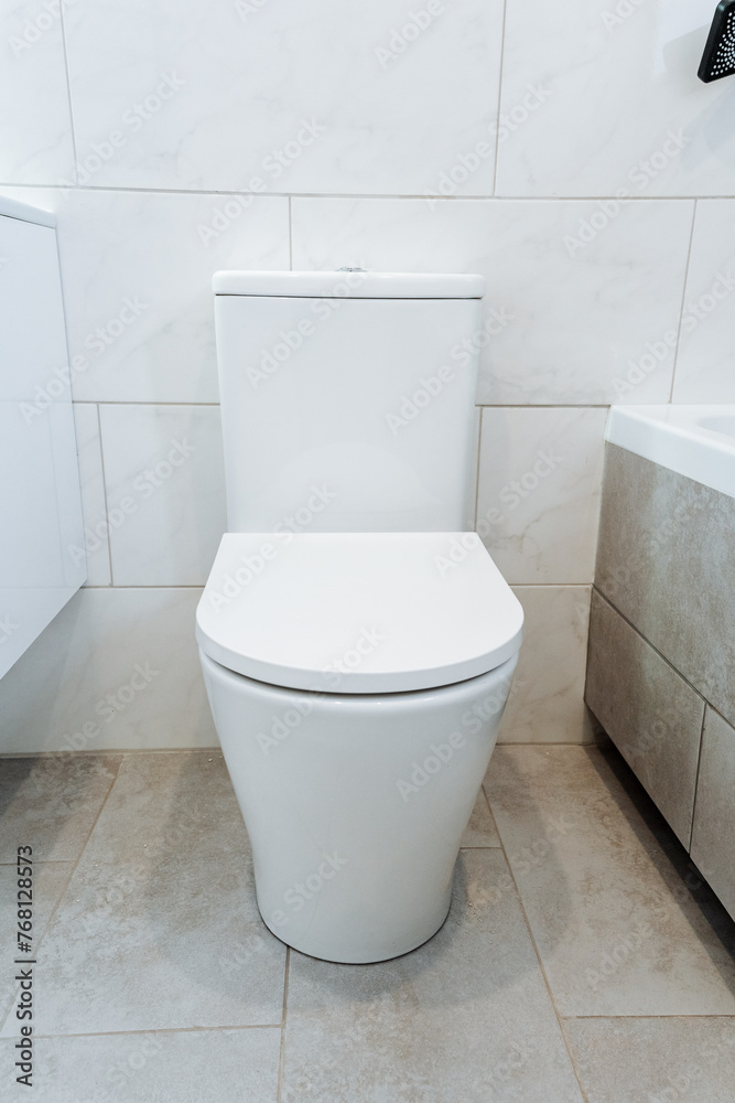 White toilet fixture in bathroom beside bathtub on ceramic flooring White toilet fixture in bathroom beside bathtub on ceramic flooring