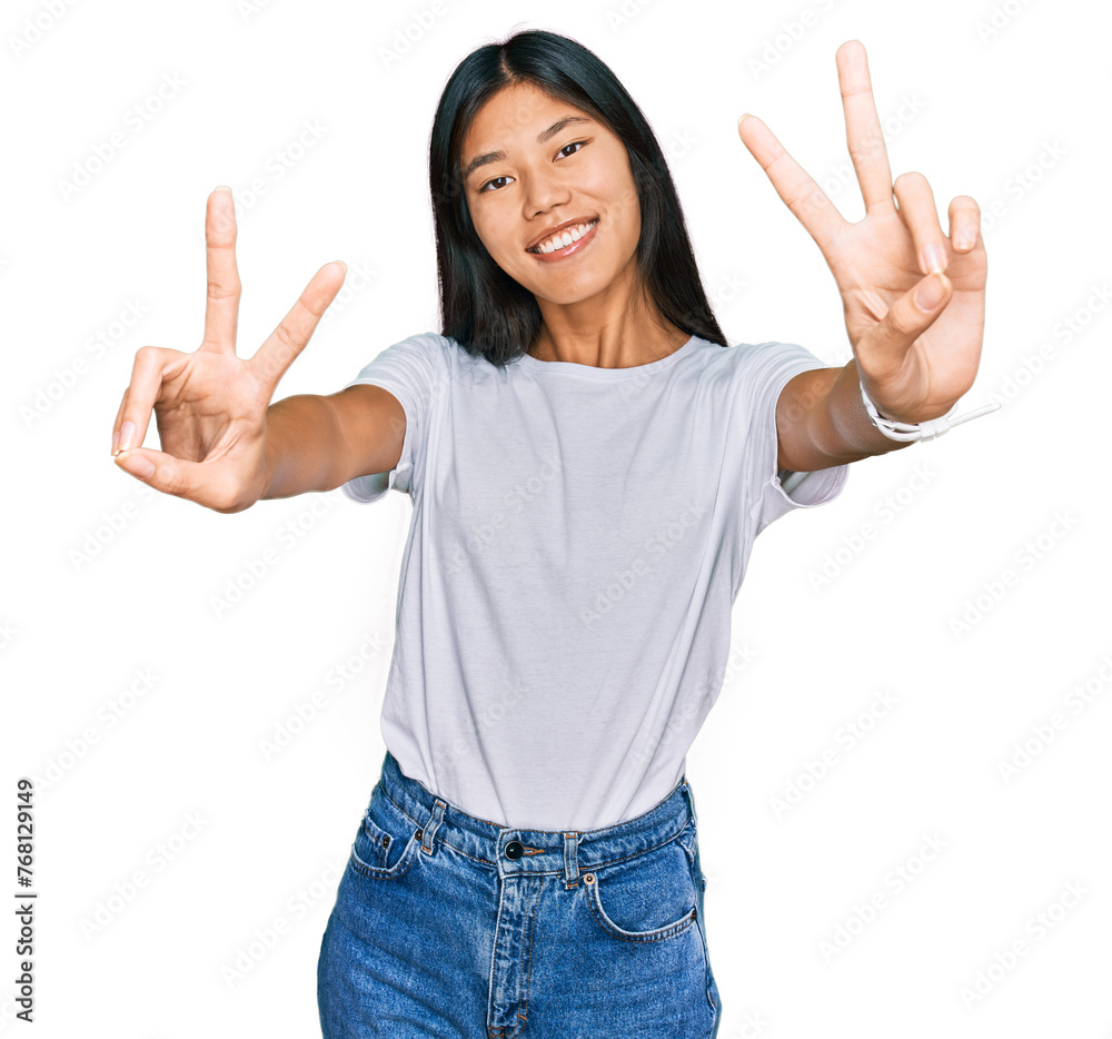 Beautiful young asian woman wearing casual white t shirt smiling with tongue out showing fingers of both hands doing victory sign. number two. Beautiful young asian woman wearing casual white t shirt smiling with tongue out showing fingers of both hands doing victory sign. number two.