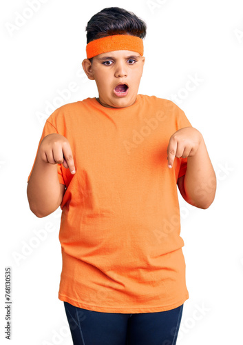 Little boy kid wearing sportswear pointing down with fingers showing advertisement, surprised face and open mouth