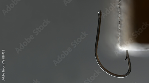 A steel fishhook is stuck into a glowing object. On a gray background.