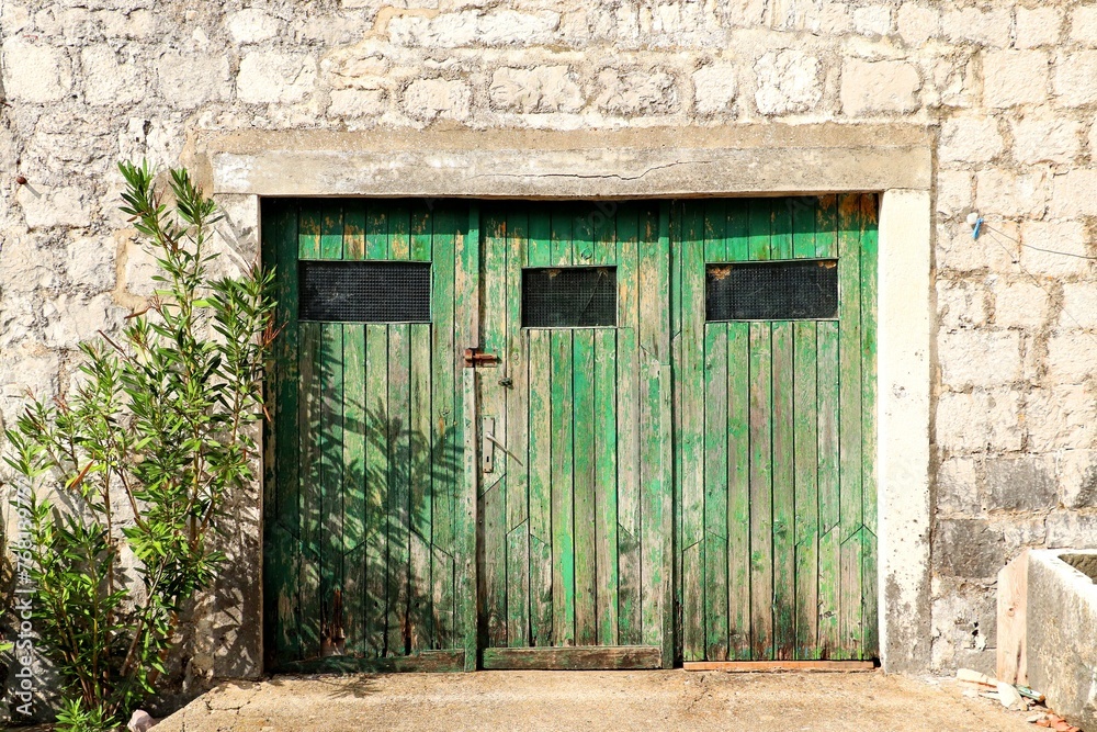 Wooden doors of an old stone house covered with flying green paint Wooden doors of an old stone house covered with flying green paint