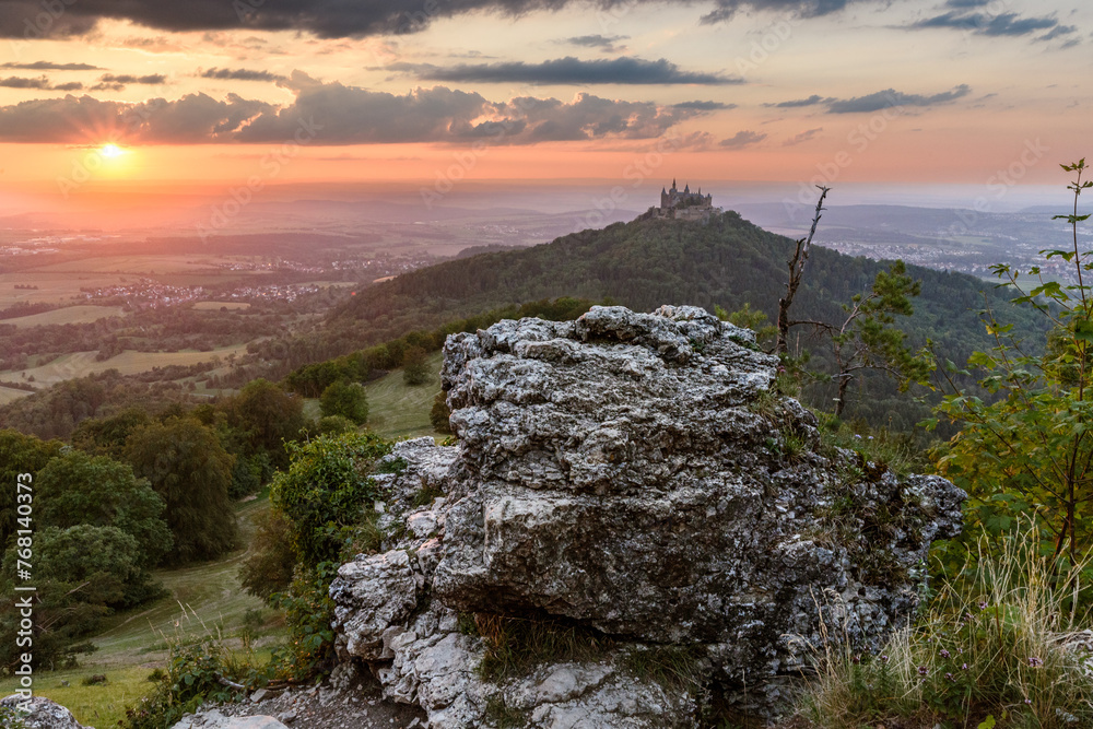 Ein blutroter Sonnenuntergang über der Burg Hohenzollern mit einem großen Fels im Vordergrund