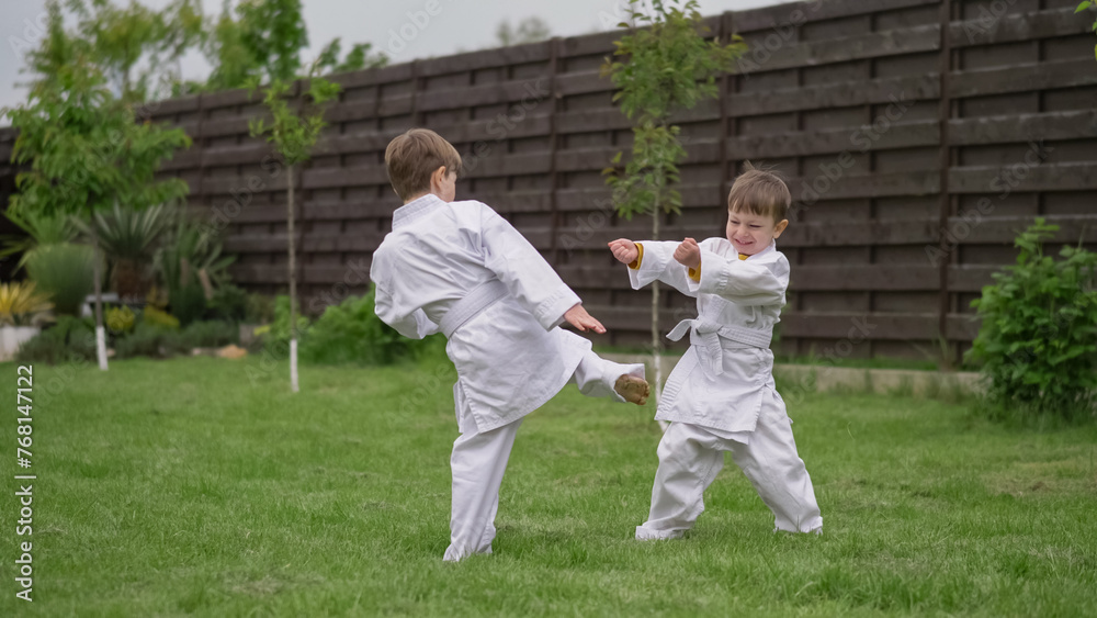 Little cheerful funny kids playing karate in white suit in the garden