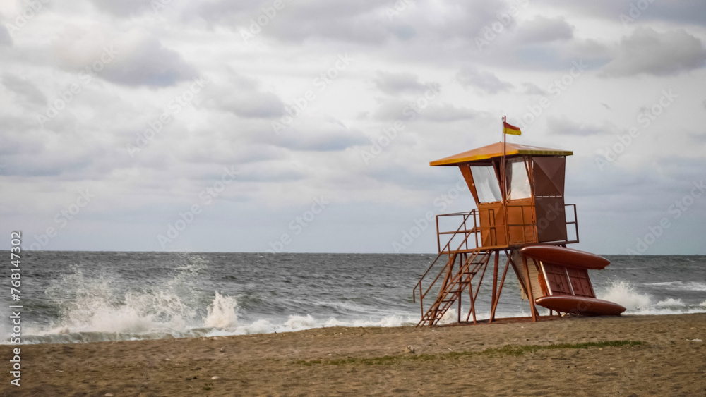 Lifeguard observation desk with red flag in front of wild sea waves on bad weather