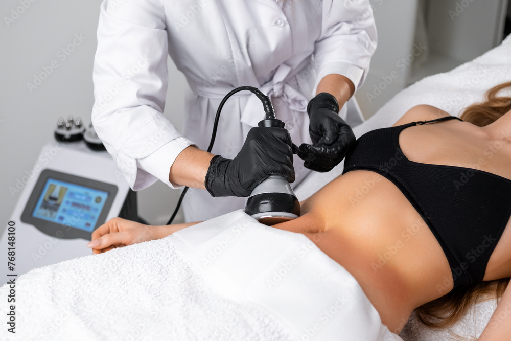 Engaging in ultrasound cavitation therapy for body contouring and anti cellulite treatment, a young woman benefits from hardware cosmetology techniques aimed at sculpting her body.