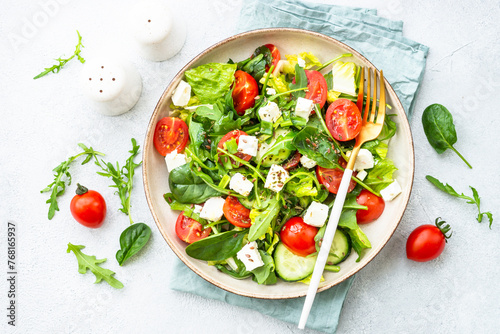 Green salad with spinach, arugula and tomatoes with olive oil. Top view on white.