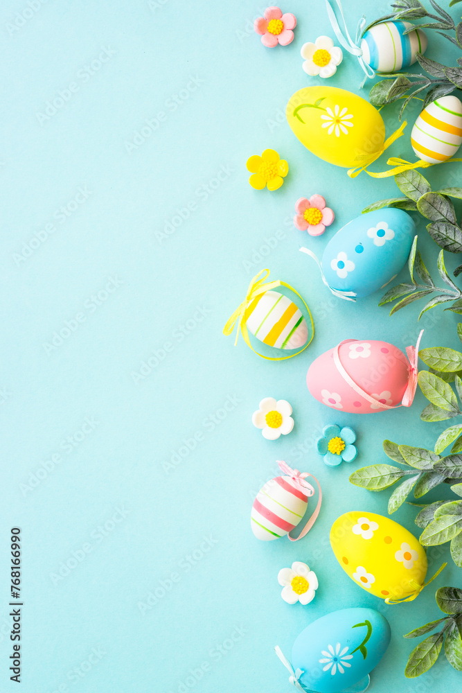 Easter background or greeting card on blue. Eggs, spring leaves, flowers and colored butterflies. Flat lay with copy space.