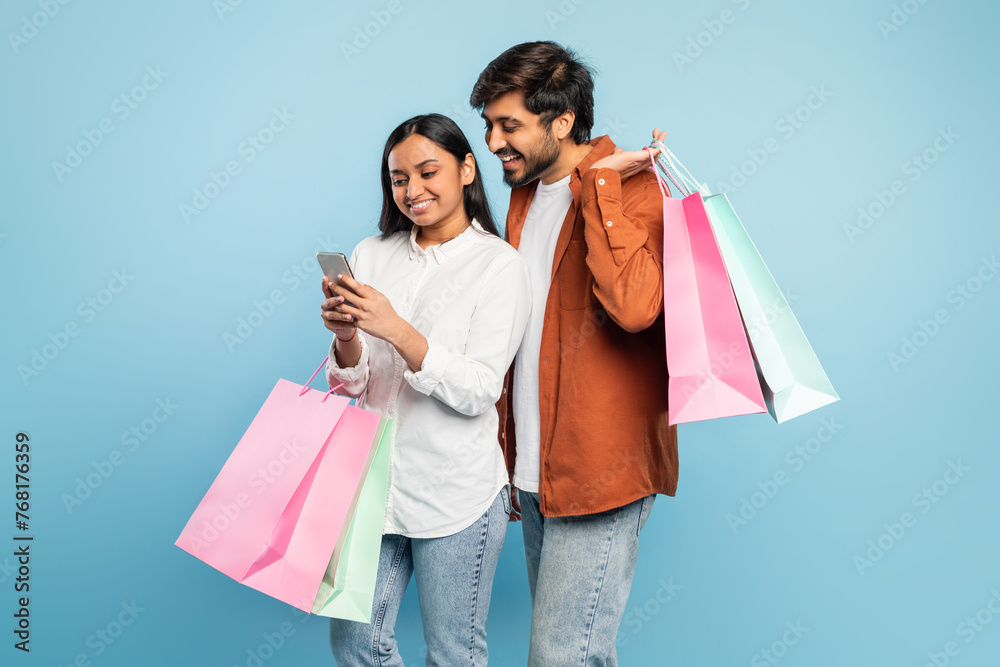 Indian couple with purchases in bags and cellphone in studio