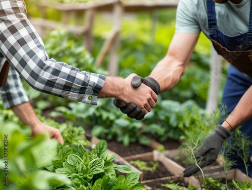 Two men shake hands in a garden. One of them is wearing a plaid shirt. The other man is wearing a blue apron