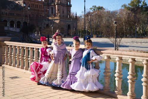 four pretty little girls dancing flamenco dressed in typical gypsy costume pose in a famous square in seville, spain. Photo taken from the side. Flamenco, cultural heritage of humanity.