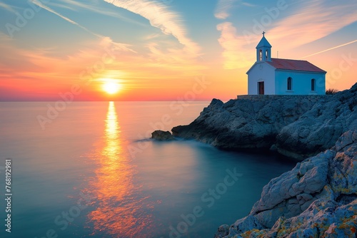 A small white church sits atop a cliff overlooking the ocean at sunset.