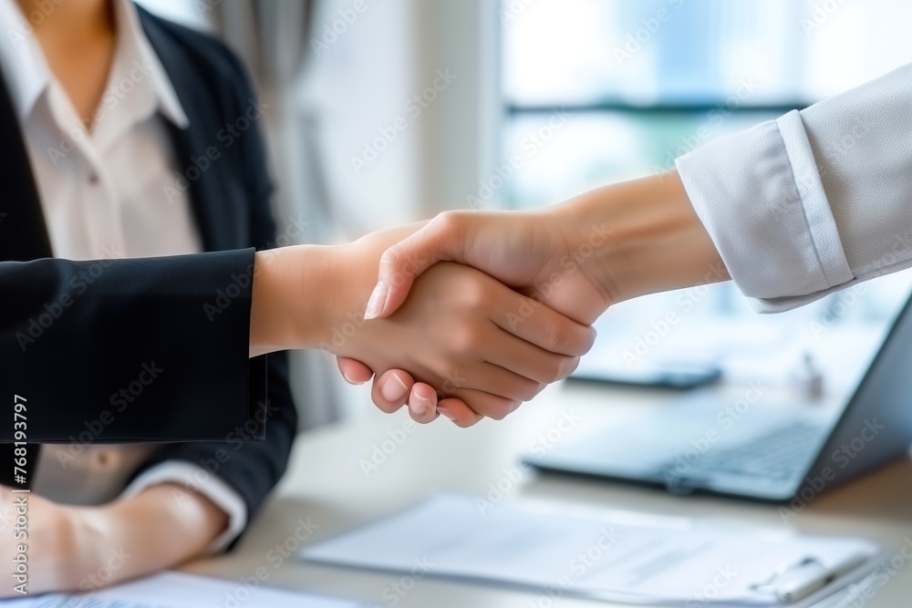 Two business women shaking hands in front of a laptop screen. Two business women shaking hands in front of a laptop screen.