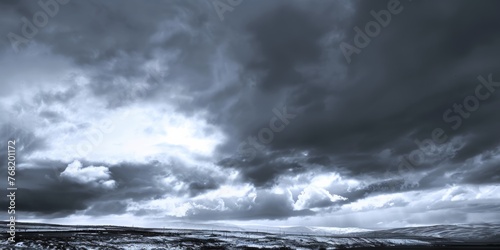A black and white image showing a dramatic grey sky filled with billowing clouds