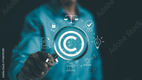 Digital copyright or patent concept. Author rights and patented intellectual property. Businessman holding a magnifying glass focuses on a copyright symbol surrounded by legal icons. trademark license photo