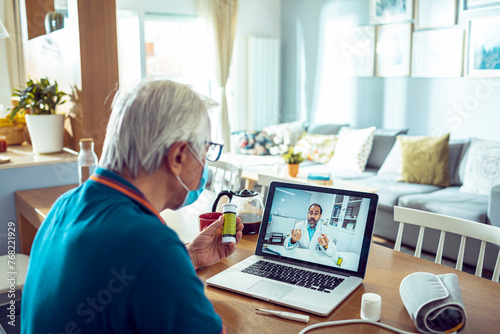 Senior man having an online consultation with a doctor while wearing face masks at home photo