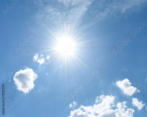 An outdoor image of a blue sky  puffy white clouds  and a bright sun