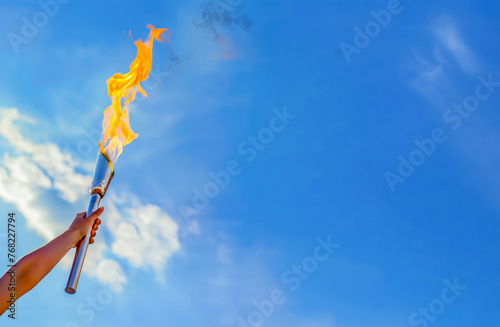 Female Athlete Arm Holding Olympic Torch with a Blue Sky Background
