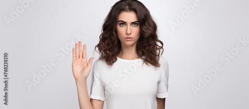 A woman in a white Tshirt is using her hand to make a stop gesture, her shoulder and neck visible as her sleeve falls down. The elegant gesture contrasts with her casual fashion design photo