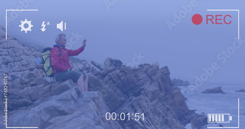 Smartphone image interface screen over caucasian senior man sitting on coast filming sea view