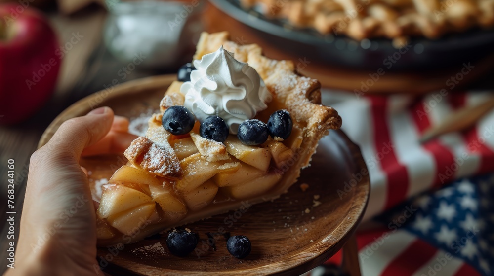 Hand holding a slice of apple pie with whipped cream and blueberries on a wooden plate.