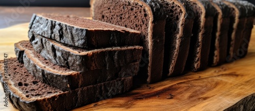 A dark and satisfying triple-layered black homemade bread is perfectly sliced and arranged on top of a wooden cutting board. photo